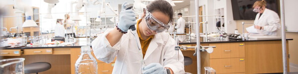 Female chemistry student conducts extracts liquid from a beaker in a lab.