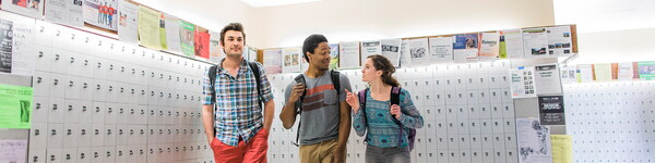 Three students in front of a wall of mail boxes.