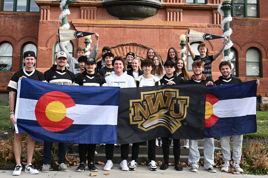 A group of students from Colorado hold up two Colorado flags and one NWU flag.