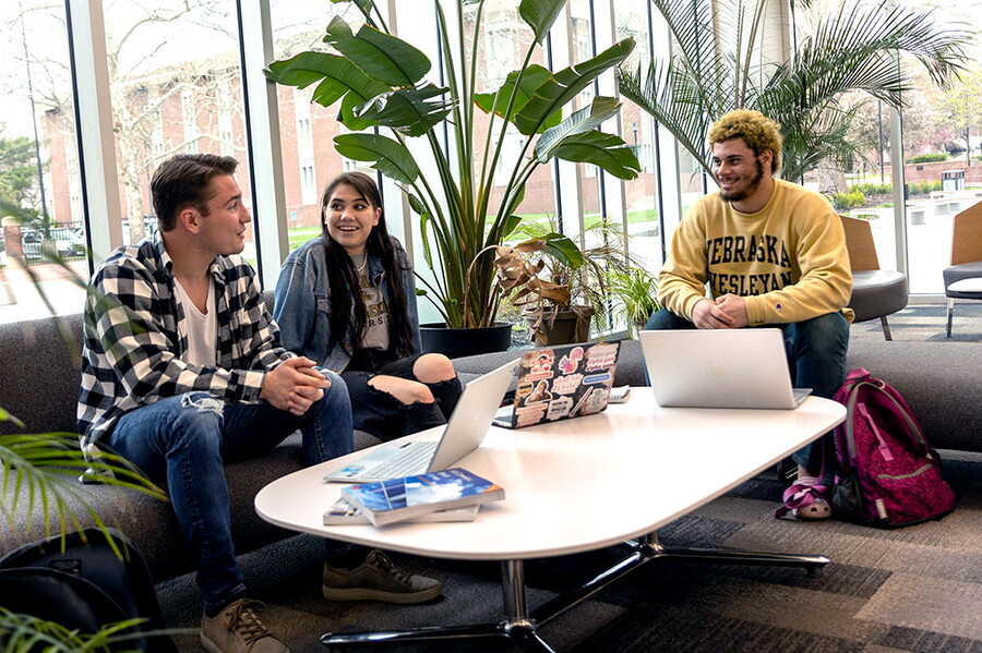 Three students study in the lobby of the Acklie building at a table.